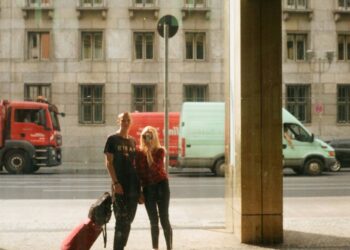 couple of unrecognizable travelers with suitcase on pavement in city