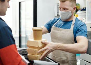man wearing a face mask putting food on a thermal bag