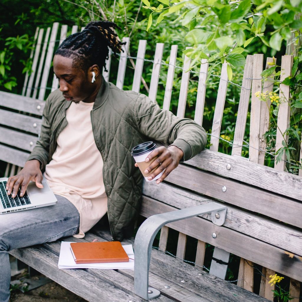 young student with coffee to go using laptop in park