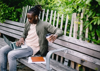 young student with coffee to go using laptop in park
