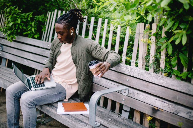 young student with coffee to go using laptop in park