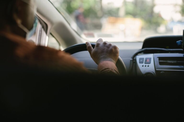 crop ethnic man driving vehicle in town