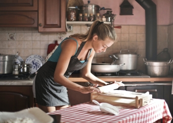 young woman rolling dough for baking in kitchen