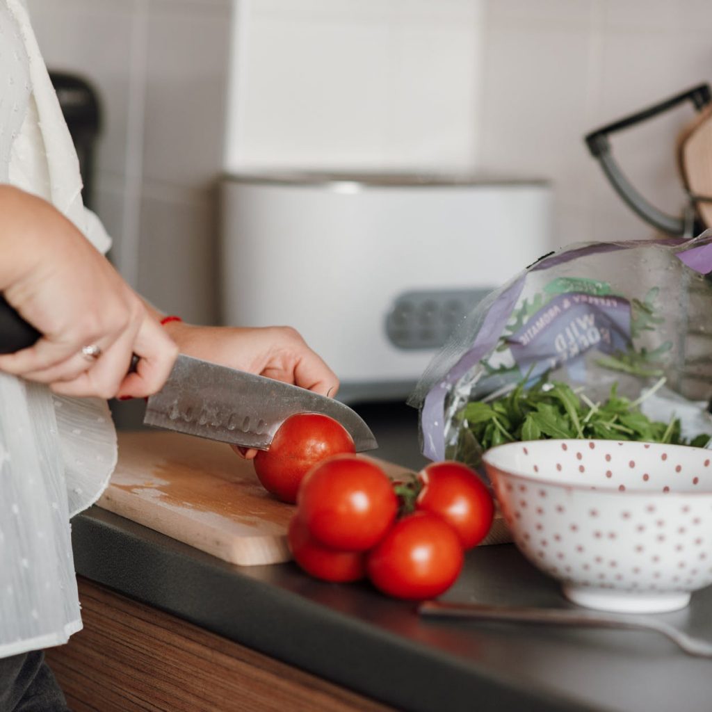 crop woman cutting tomatoes in kitchen