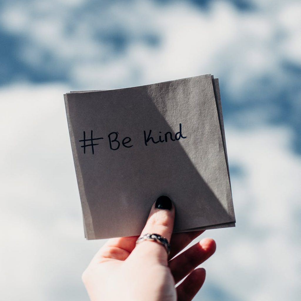 person holding note with be kind text