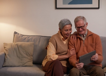 man and woman sitting on sofa while looking at a tablet computer