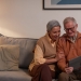 man and woman sitting on sofa while looking at a tablet computer