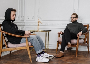 man in black sweater and blue denim jeans sitting on brown wooden chair