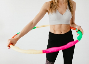 crop sportswoman exercising with gymnastic hula hoop