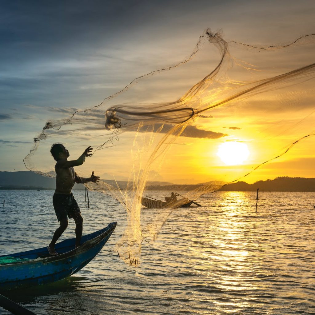 person throwing fish net while standing on boat