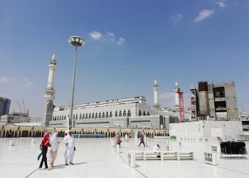 unrecognizable muslim pilgrims near ancient mosque on sunny day