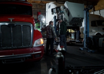 man in black jacket standing beside red car