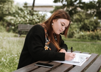 concentrated woman writing notes in papers in park
