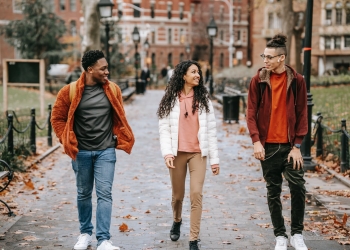 positive young ethnic guys with female friend walking along pathway in city