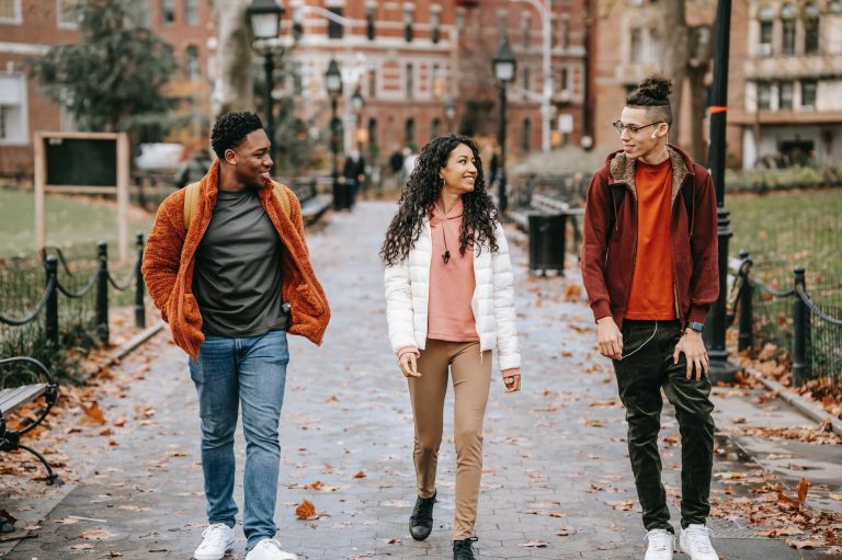 positive young ethnic guys with female friend walking along pathway in city