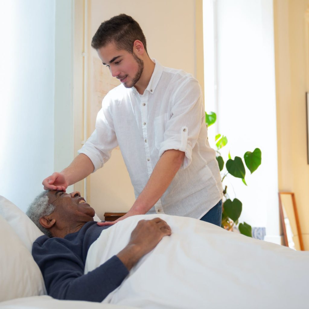 a man in white shirt standing beside an elderly lying on the bed