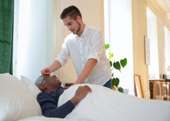 a man in white shirt standing beside an elderly lying on the bed