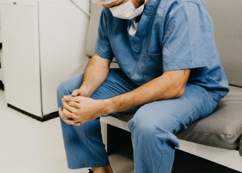 man wearing blue scrub suit and mask sitting on bench