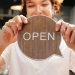 happy woman showing wooden signboard saying open