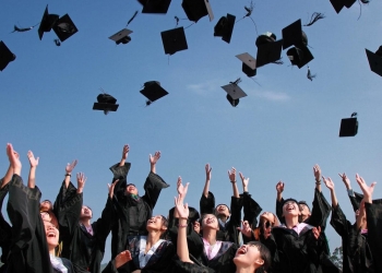 newly graduated people wearing black academy gowns throwing hats up in the air