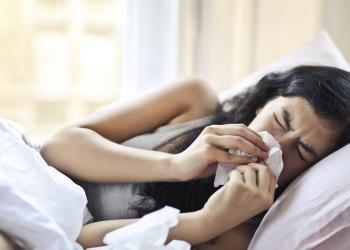 woman lying on bed while blowing her nose