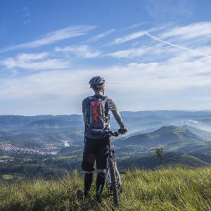 biker holding mountain bike on top of mountain with green grass