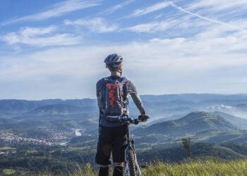 biker holding mountain bike on top of mountain with green grass