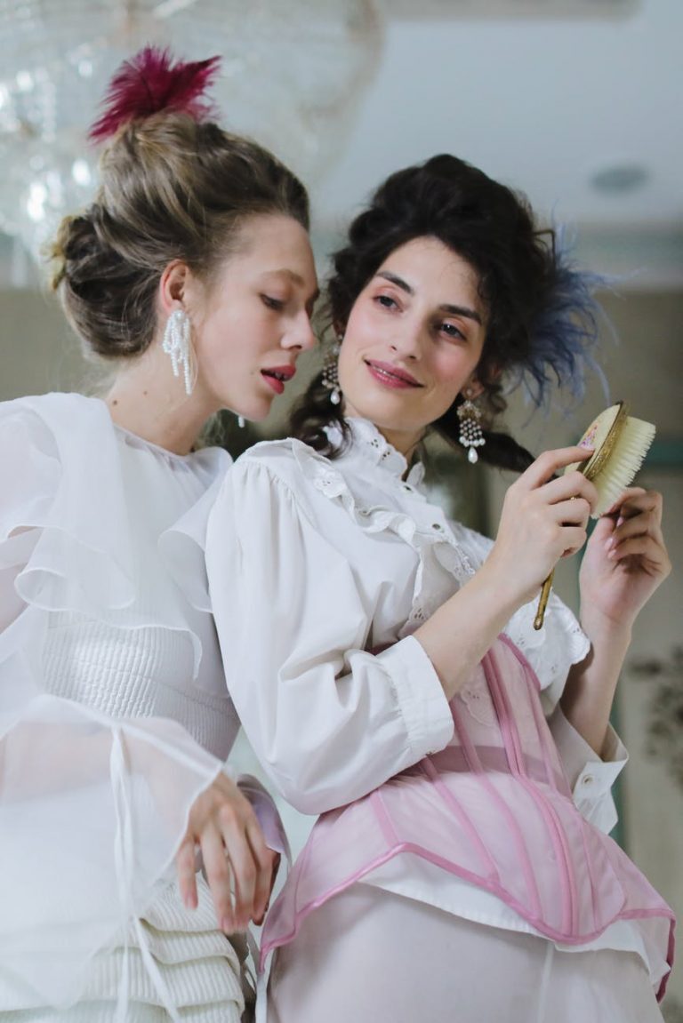 woman wearing white and pink dress brushing her hair beside woman in white dress