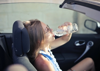adult female drinking water in convertible car in city