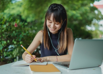 happy young asian student doing homework and listening to music with earphones
