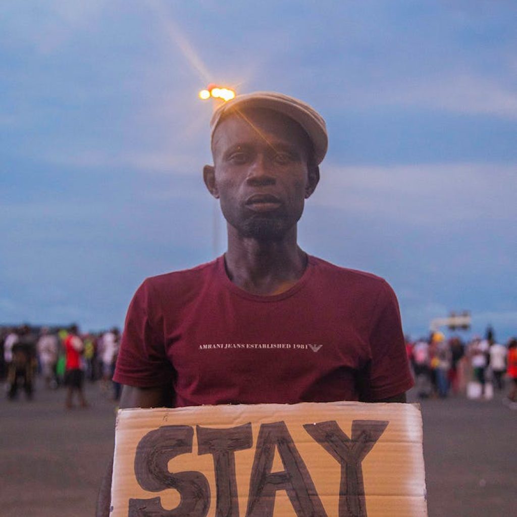 man wearing a hat holding a placard with a text stay woke