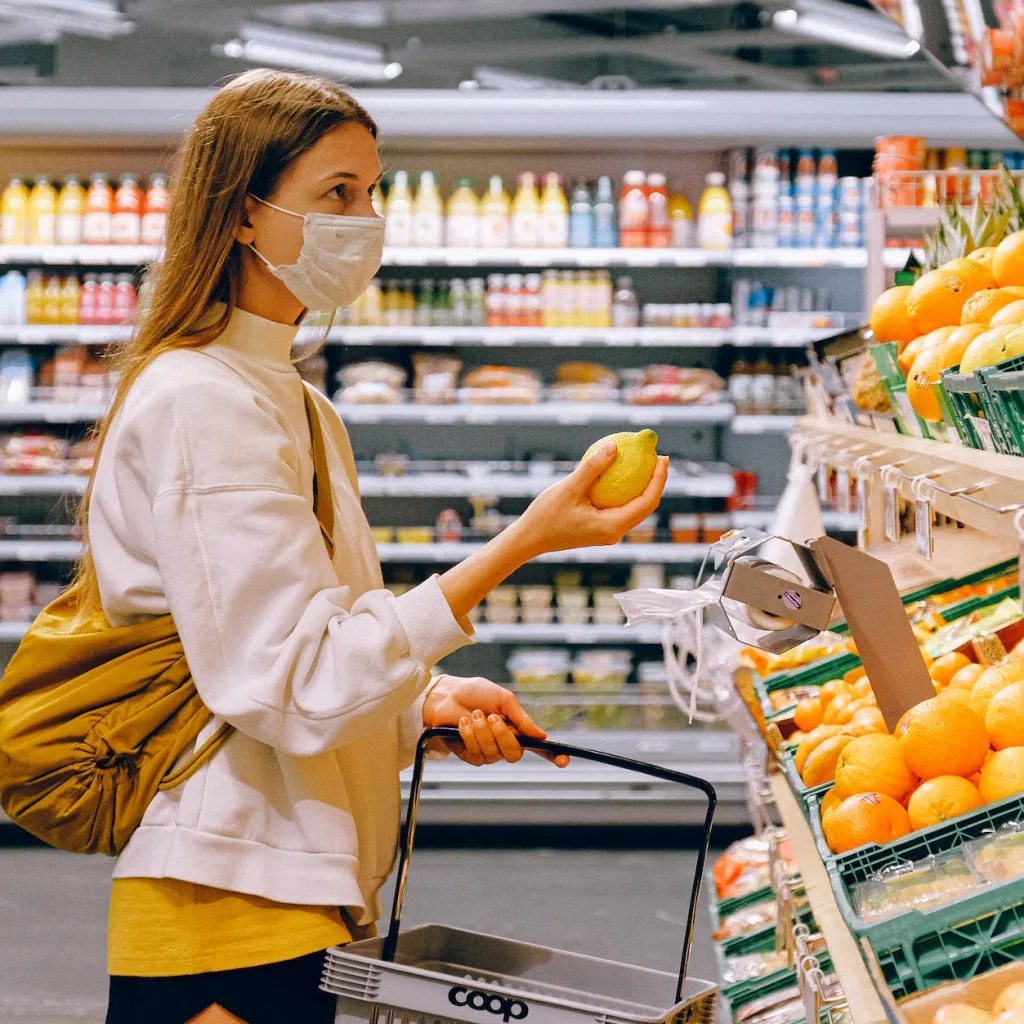 woman in yellow tshirt and beige jacket holding a fruit stand