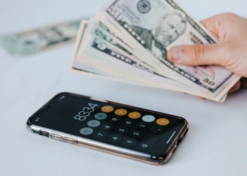 crop faceless person with cash and calculator app on smartphone