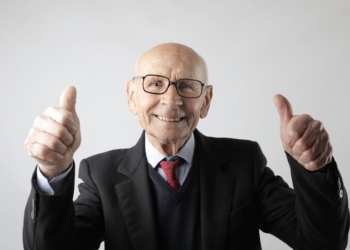 positive senior man in eyeglasses showing thumbs up and looking at camera