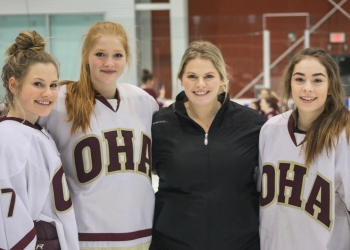 Coach Kayla Lascelle, third from the left posing with three hockey players.