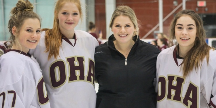 Coach Kayla Lascelle, third from the left posing with three hockey players.