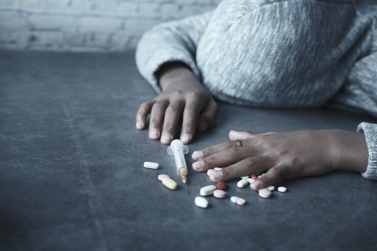 close up photo of person lying beside a syringe and tablets