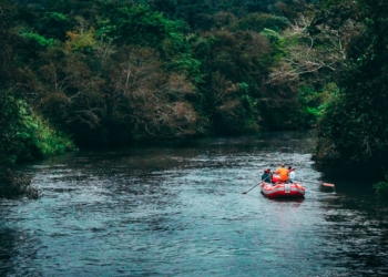three persons riding red inflatable raft