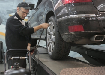 serious car mechanic pumping up car wheel in modern service garage
