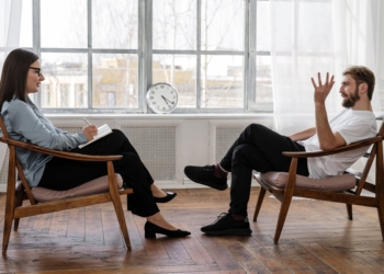 person in black pants and black shoes sitting on brown wooden chair