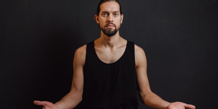 a bearded man in black tank top sitting while meditating