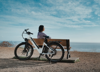 man in black shirt sitting on brown wooden bench beside black and white bicycle during daytime