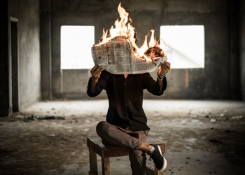 man sitting on chair holding newspaper on fire