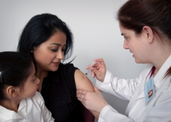 woman injecting woman's arm carrying child