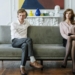 Woman in White Dress Shirt and Black Pants Sitting on Gray Couch