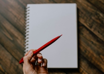 person holding red pencil writing on white paper