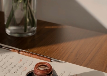 A Bottle of Ink and a Quill Lying on a Page with a Handwritten