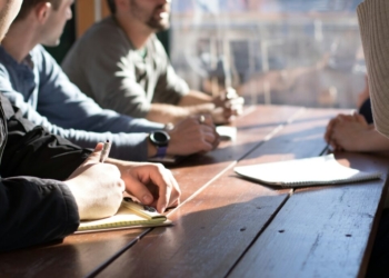 people sitting on chair in front of table while holding pens during daytime