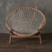 Empty simple round cane chair placed on wooden floor near gray wall in light room