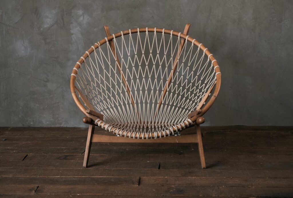 Empty simple round cane chair placed on wooden floor near gray wall in light room